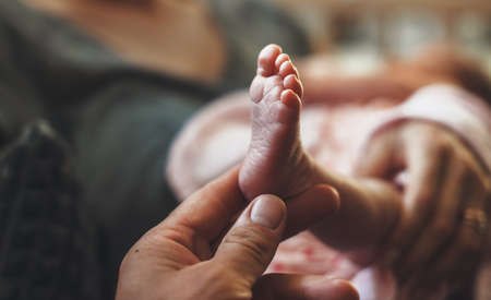 Newborn babys leg held by his father and shown at camera after coming home
