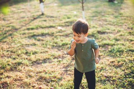 small caucasian boy smiling and playing on green grass in park during walk in a summer dayの写真素材