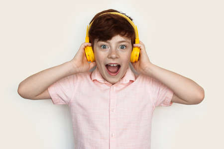 Amazed caucasian ginger boy wearing headphones listening to music on a white studio wallの写真素材