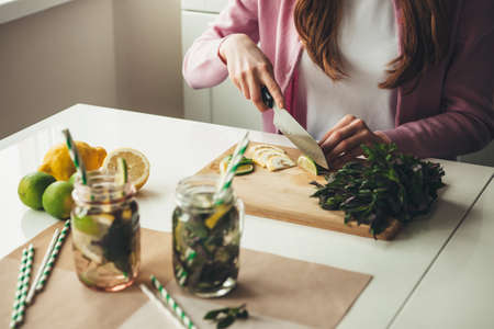 Caucasian woman slicing fruits for making a mojito drink at home using lemons and mint in jarの写真素材