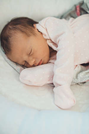 Caucasian newborn girl sleeping in pink clothes lying on a soft white blanketの写真素材