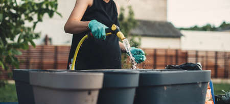 Pregnant caucasian woman is watering some flower pots while working in the garden at home