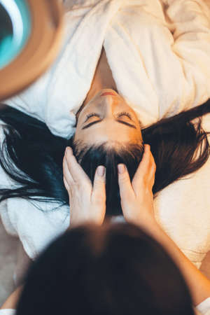 Upper view photo of a brunette woman lying at spa salon having a head massage procedureの写真素材