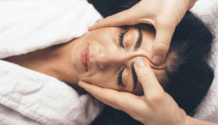 Brunette woman having facial anti aging massage at the spa salon while lying with closed eyesの写真素材