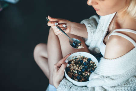Upper view photo of a caucasian woman in a knitted sweater eating cereals with berry at homeの写真素材