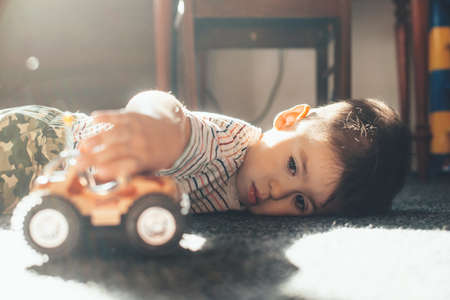 Caucasian boy lying on the floor and playing with a toy car during a sunny dayの写真素材