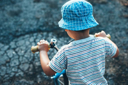 Upper view photo of a caucasian boy riding the bike and wear a hat in a summer dayの写真素材