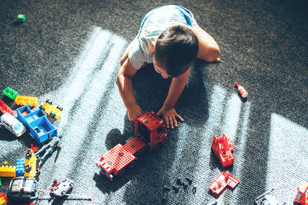 Upper view photo of a caucasian boy playing with constructor car while sitting on the floor and practice self developingの写真素材