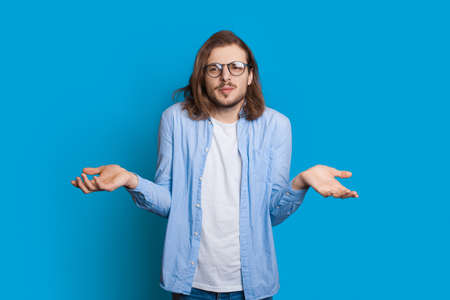 Confused caucasian man with beard and long hair is posing indecisive while gesturing with palms on a...