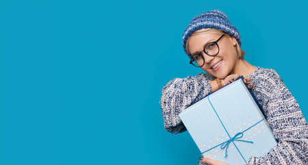Close up photo of a caucasian woman with glasses and hat posing with a gift near blue studio free...