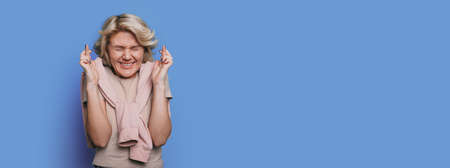 caucasian blonde woman is praying and begging for something on a blue studio wall with free space...