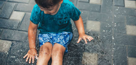 Upper view photo of a caucasian boy playing in the ground in water wearing blue clothes in the backyardの写真素材