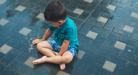 upper view photo of a caucasian boy playing with water on the ground after a rainの写真素材