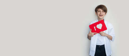 Adorable boy is holding a paper with like sign while advertising something on a gray studio wallの写真素材