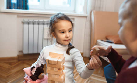 Caucasian little charming girl playing  with her mother and teddy bear holding a wooden blockの写真素材