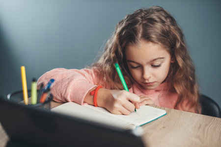 close up photo of a curly haired girl drawing something while watching videos on tabletの写真素材
