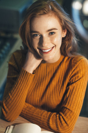 Close up photo of a ginger woman with freckles smiling at camera while reading a bookの写真素材