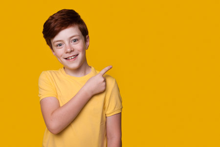 Caucasian ginger boy is advertising something pointing at the yellow studio free spaceの写真素材