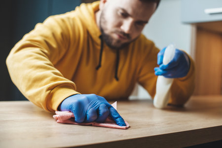 Bearded man with special spray is cleaning the house and disinfecting it during the pandemic...
