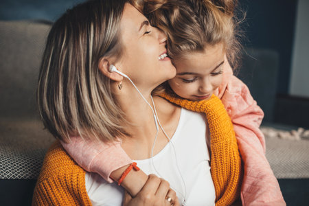 Charming girl embracing her mother while she is listening to music on the floor