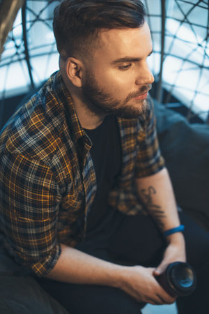 Caucasian man posing thoughtful on a couch with a coffee cup looking and meditating on somethingの写真素材