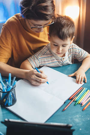 Upper view photo of a careful mother helping her son doing the homework writing something in the copybookの写真素材