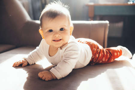 Adorable newborn kid is smiling at camera while lying on the couch in a sunny day