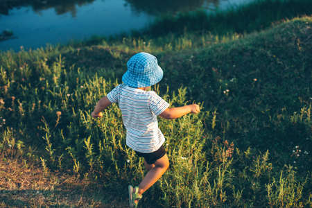 Caucasian boy is running and jumping in a field near a river playing in a summer eveningの写真素材