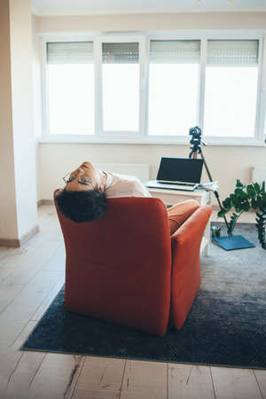 Young caucasian woman is lying on a couch gesturing tiredness while having online video lessonの写真素材