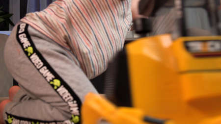 Close up photo of a boy on the floor driving a toy car near his newborn sister