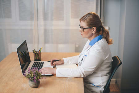Senior blonde doctor at the office using a laptop during the working day