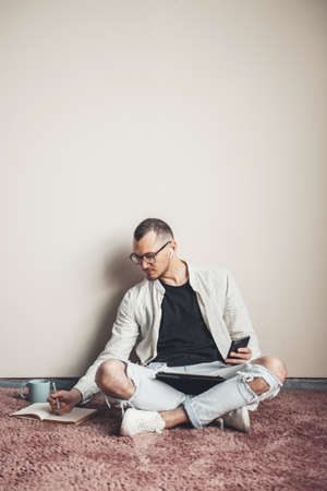 concentrated freelancer using tablet and phone write working at home on the floor having a coffee