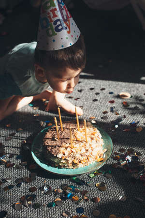 Caucasian small boy wearing a party cap is blowing the lights on the cake celebrating birthdayの写真素材