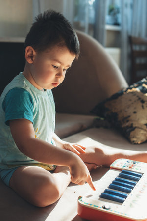 Caucasian small kid is trying to play toy piano on the floorの写真素材