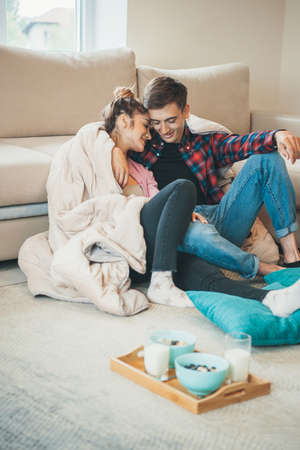 Adorable couple are embracing on the floor near the couch before eating cereals with milkの写真素材