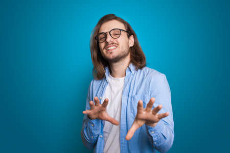 Modern man with beard gesturing hands on blue background. Greeting concept. Success concept....