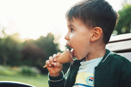 Beautiful portrait of small baby eating icecream in park on bench. Outdoor summer fun. Sweet food.