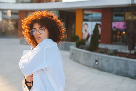 Curly businesswoman holding laptop and gesturing surprisement outside. Business people posing in sunshine.の写真素材