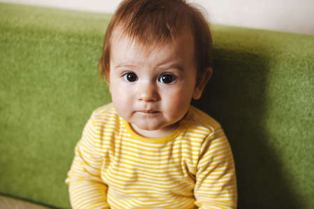 Small baby on couch looking at camera for lifestyle design. Baby siting at home. Family care. Funny...