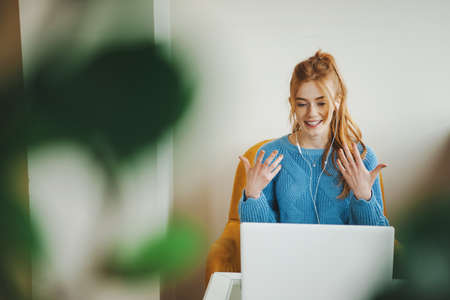 Front view of a woman actively participating in an online interview sitting on an armchair. Red hair...