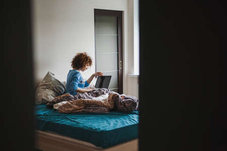 Young woman spending her morning surfing the internet. View from the half open door