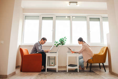 Side view of a couple working from home due to pandemic situation. Standing on the couch in front of...