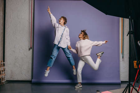 Two women in casual wears jumping on isolated purple background. Hand in hand. Friendship.の写真素材
