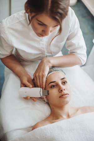 Close-up portrait of a woman receiving ultrasound cavitation facial peeling. Spa salon. Cosmetology beauty procedure.の写真素材