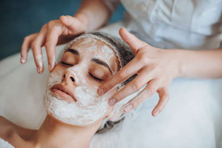Closeup portrait of cosmetologists hands applying mask on clients face in spa salon. Natural beauty. Facial skincare. Rejuvenation treatment.の写真素材