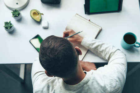 Top view of a man sitting in a chair at the office table and writing homework. Education, school concept.の写真素材