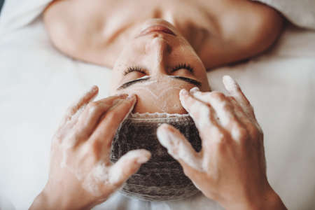 Top view. Cleaning woman face with foam, a caucasian woman in spa salon. Cosmetologist job.の写真素材
