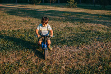 Front view of a caucasian boy riding a bike in a field. Healthy lifestyle. Outdoor summer fun. Outdoor recreation. Sport play. Green grass field.の写真素材