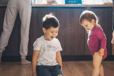 Two kids daughter and son having fun playing toys on kitchen floor. Kids play. Babygirl.の写真素材