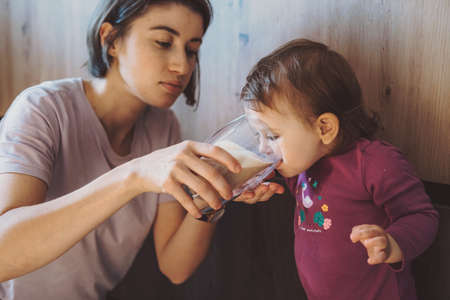 Mother giving the girl a glass of milk to drink. Maternal care. Childhood.の写真素材